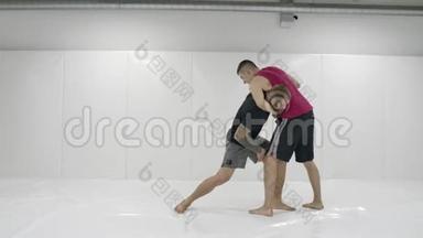 在一间白色的房间里，两个男摔跤手在扔垫子。 抓住一个抓斗把自己扔出去